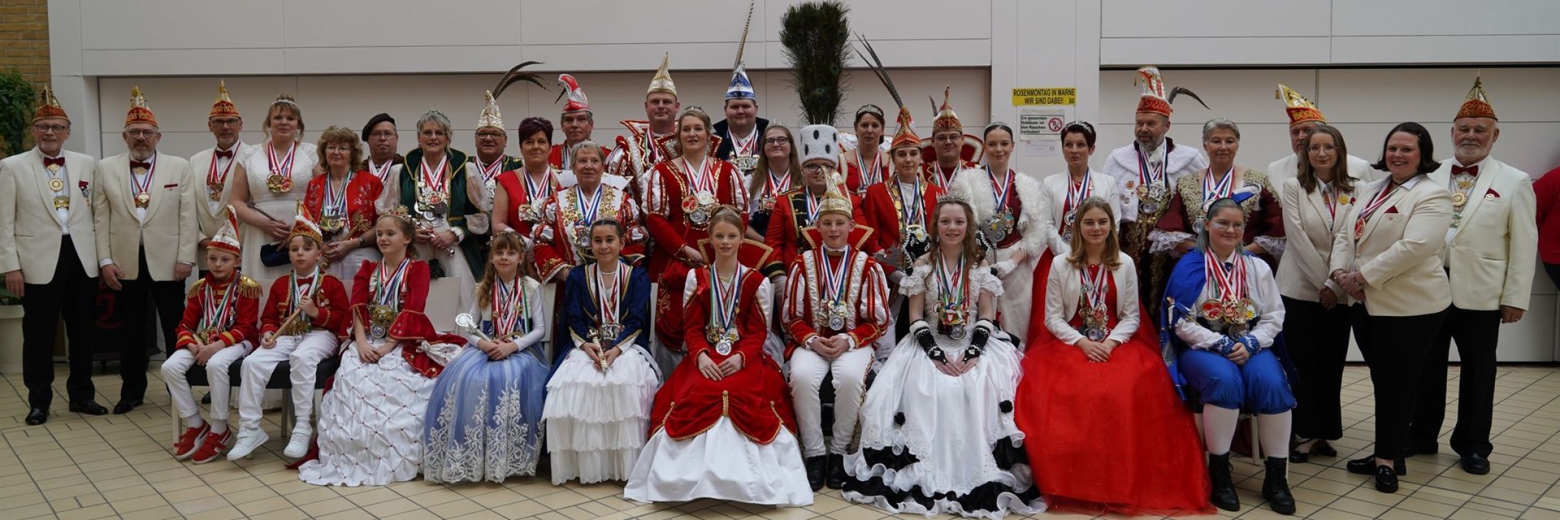 Eine große Gruppe von Menschen in farbenfrohen Kostümen posiert für ein Gruppenfoto in einer Halle.